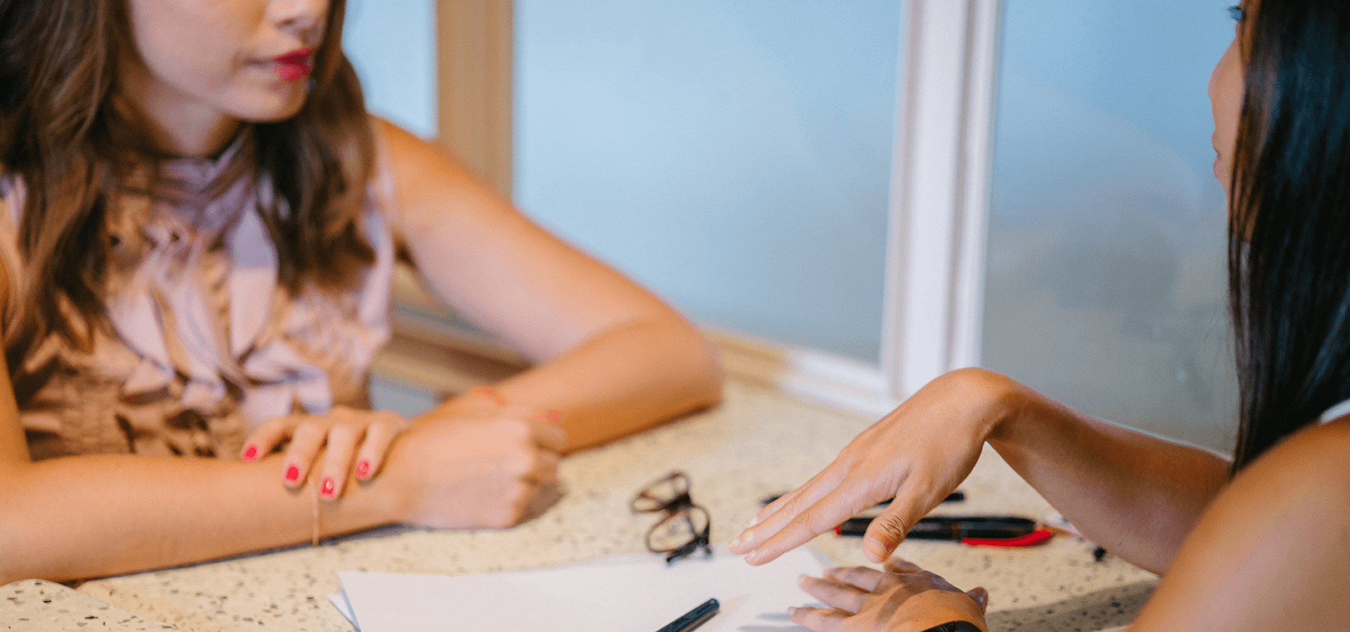 Two women having a conversation at a table with papers between them.