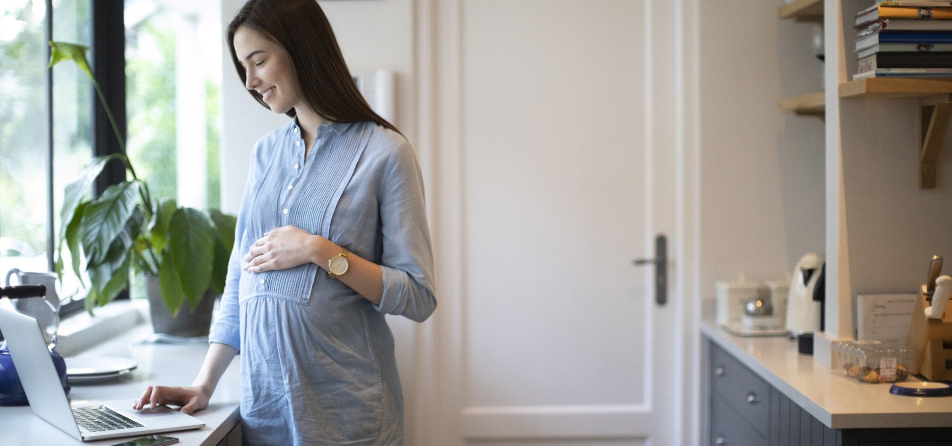 Smiling pregnant woman using laptop in kitchen