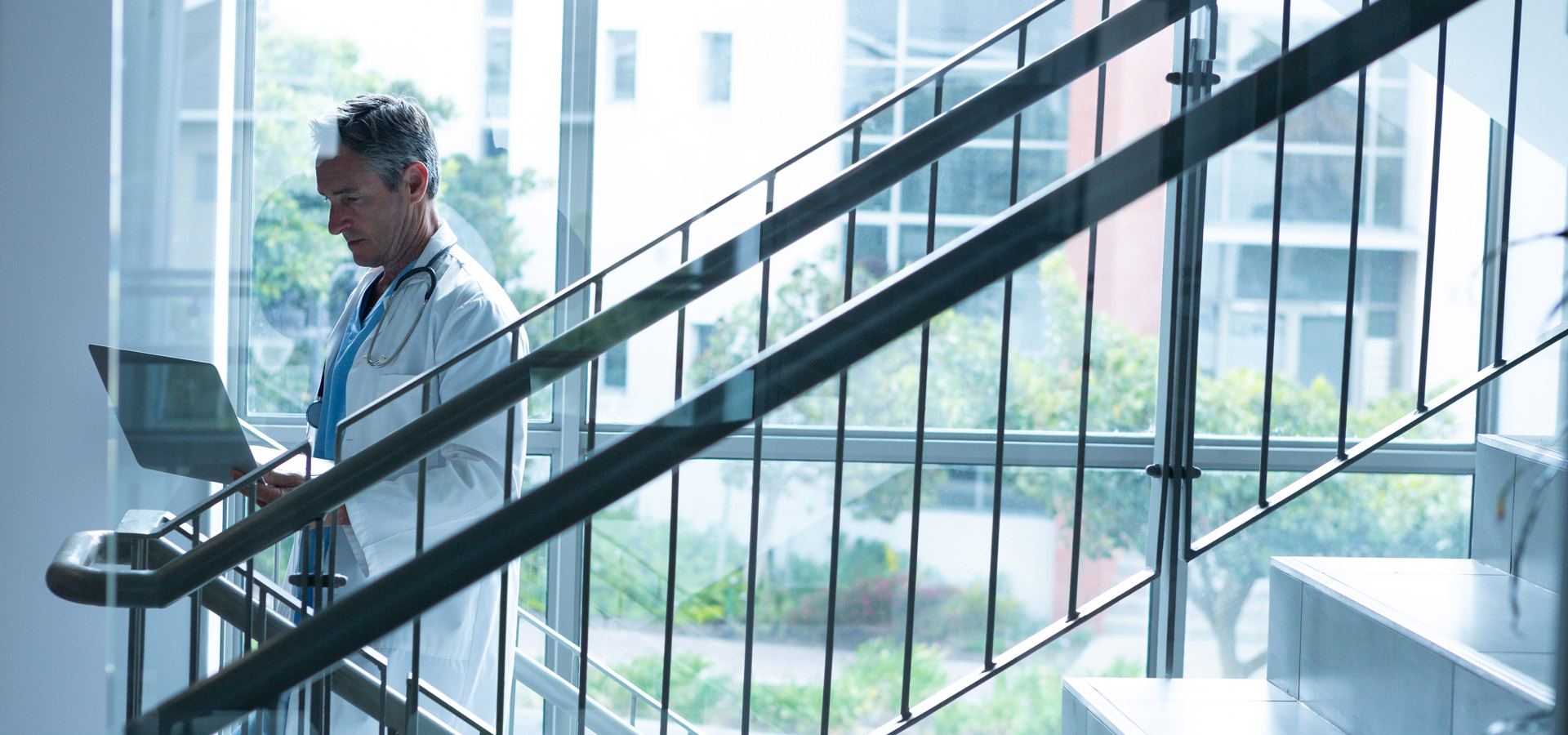 Male doctor using laptop while walking the stairs