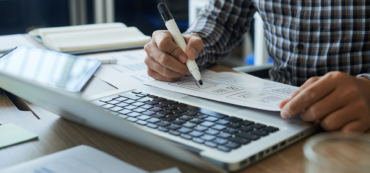 person in front of laptop making notes on paper with marker