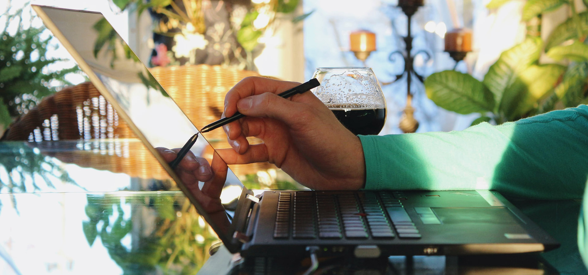 laptop on a table and a hand reaching out to touch it with a pen.