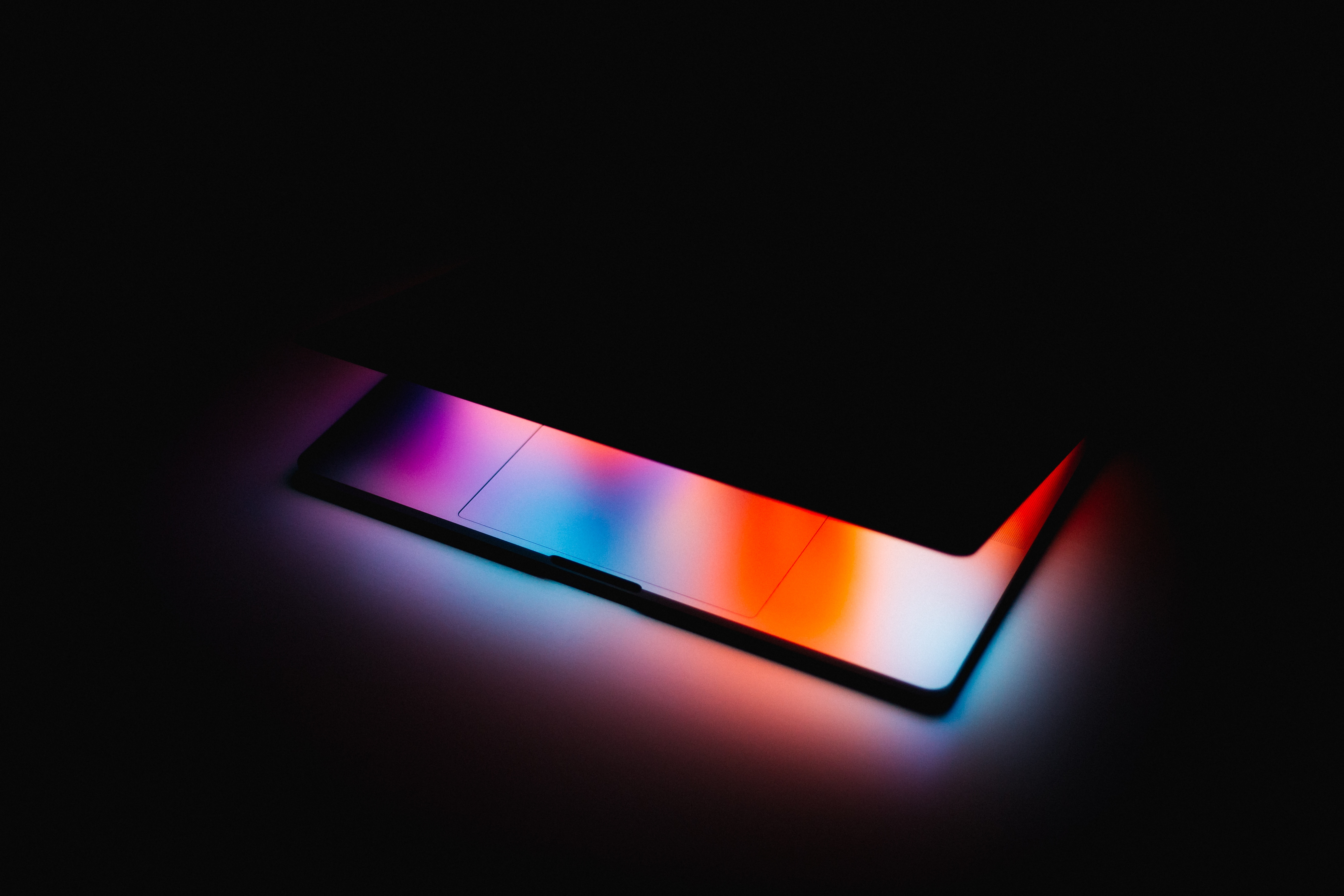 Slightly opened laptop displaying color on keyboard in dark room