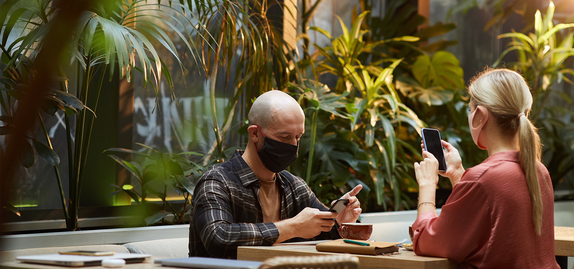 Young people in protective masks working online on mobile phone sitting in cafe